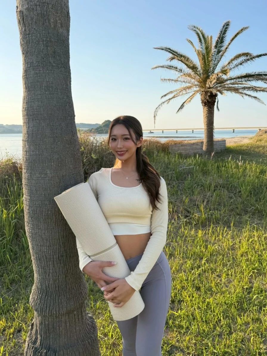 海辺でヨガマットを持ち正面を向くReona